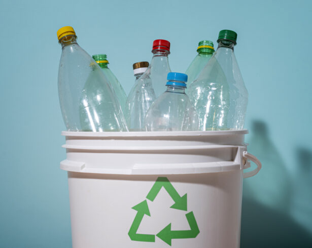 Puste plastikowe butelki w koszu z logiem recyclingu